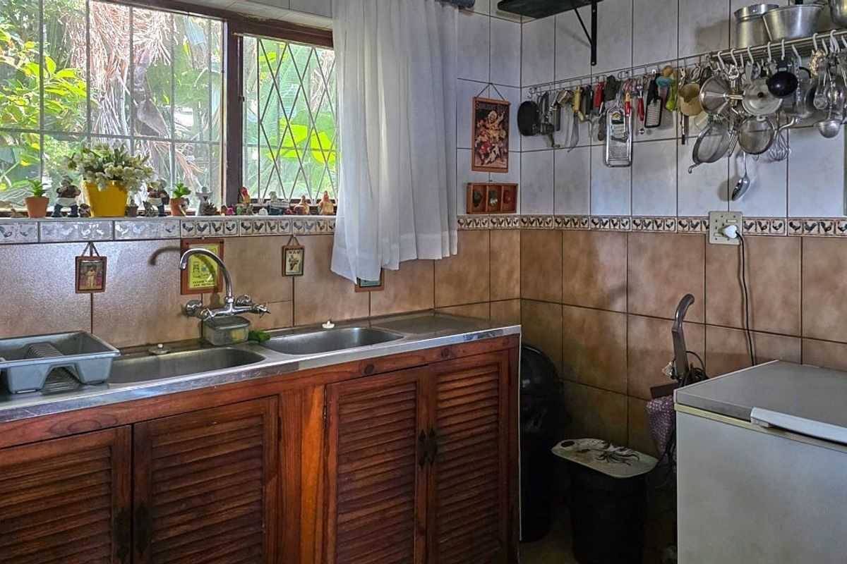 A functional kitchen area featuring wooden cabinetry, a double stainless steel sink, and tiled walls with a decorative border.