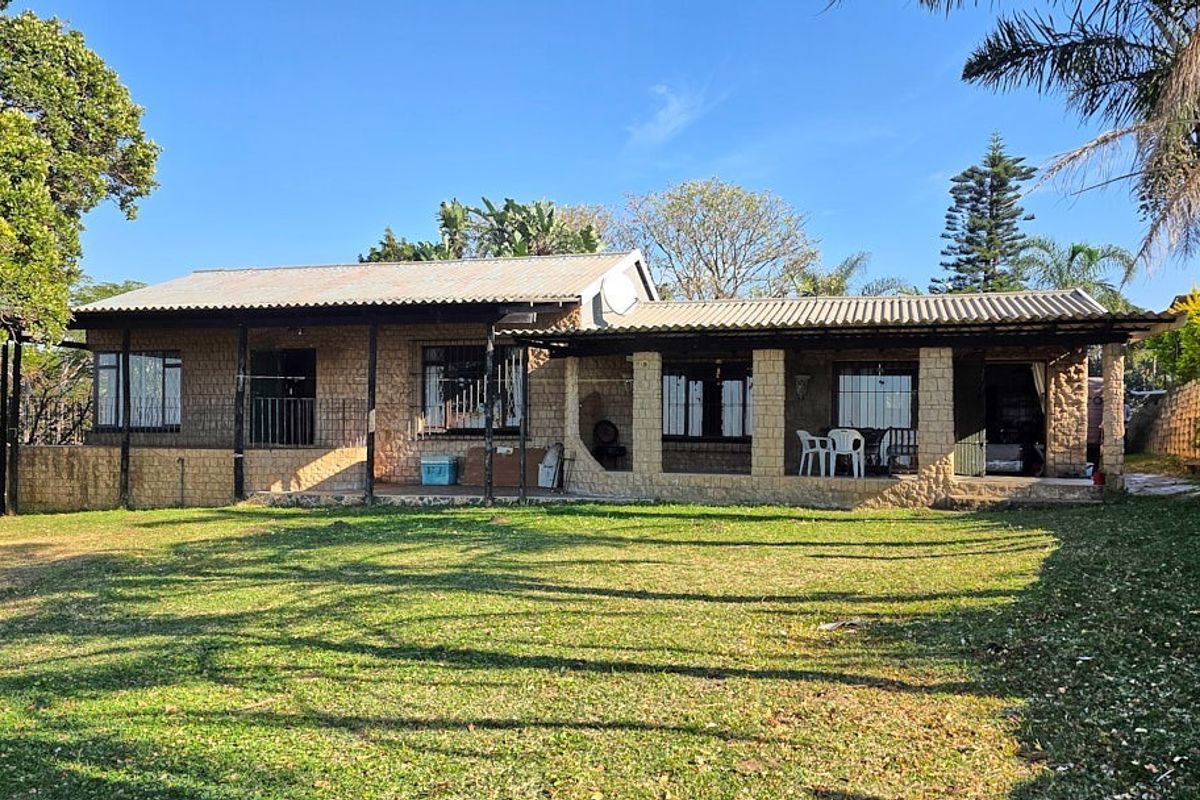 A rear view of a single-story house featuring a covered patio, stone-clad exterior walls, and a large surrounding lawn.