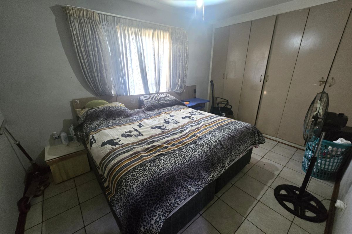 A bedroom featuring tiled flooring, built-in cupboards, and a ceiling fan, offering a functional space with potential for modernization.
