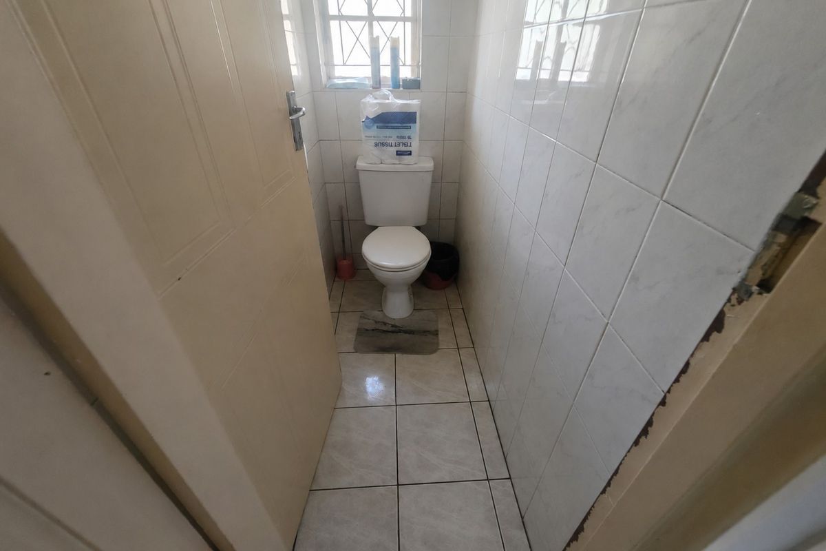 A compact guest toilet featuring tiled walls and flooring, equipped with a standard white toilet suite and a security-grille window.