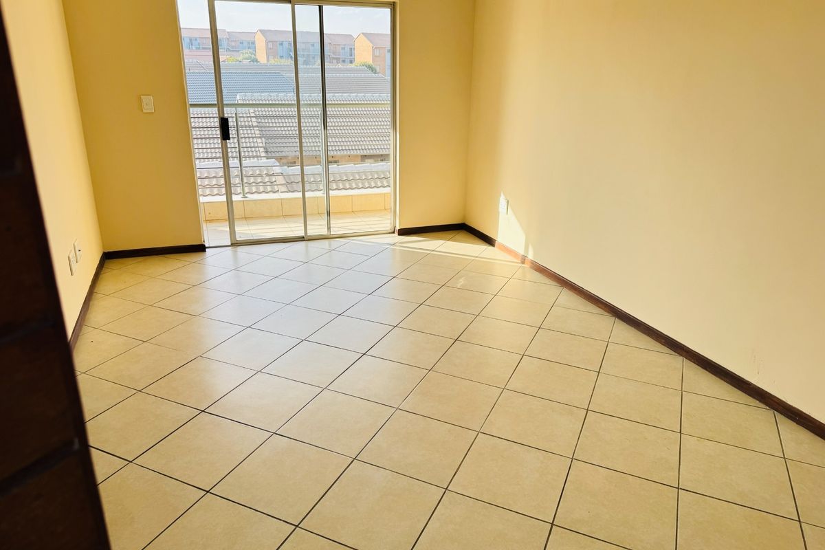 A bright, empty bedroom featuring tiled flooring and sliding glass doors that open onto a private balcony.