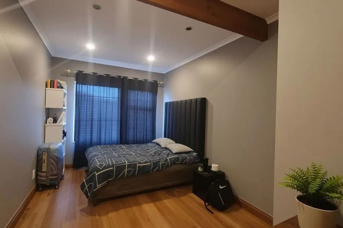 A well-maintained bedroom featuring timber-look flooring, recessed ceiling lighting, and a decorative exposed timber ceiling beam.