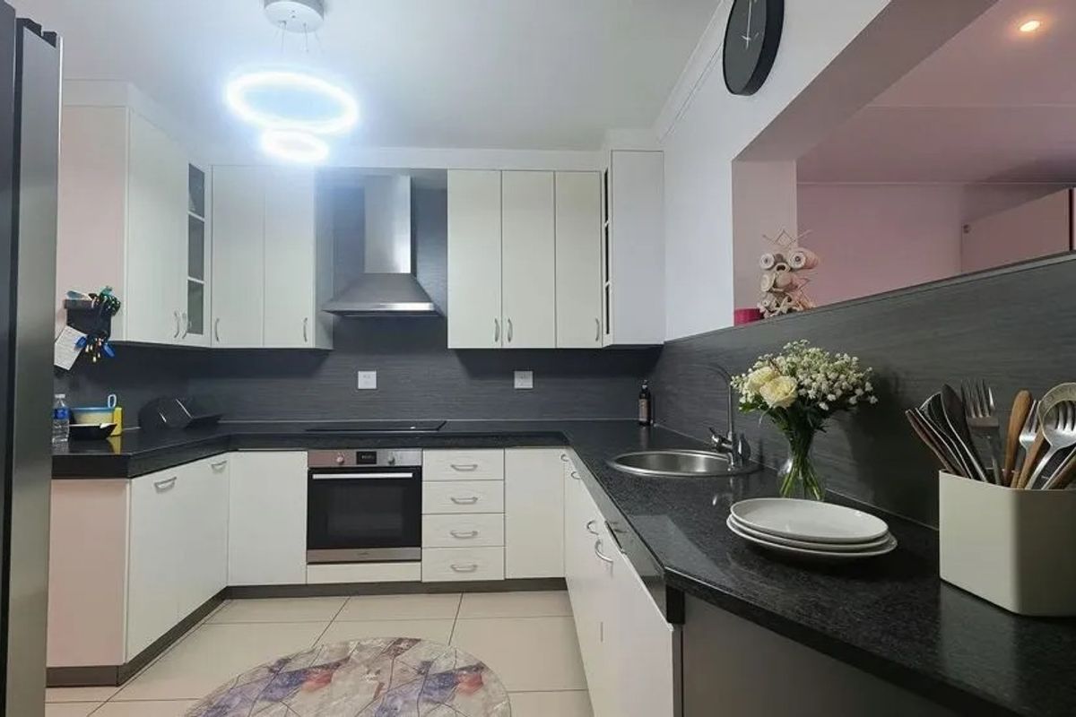 Modern kitchen featuring white cabinetry, dark stone countertops, stainless steel oven, extractor fan, and a sleek breakfast bar pass-through.
