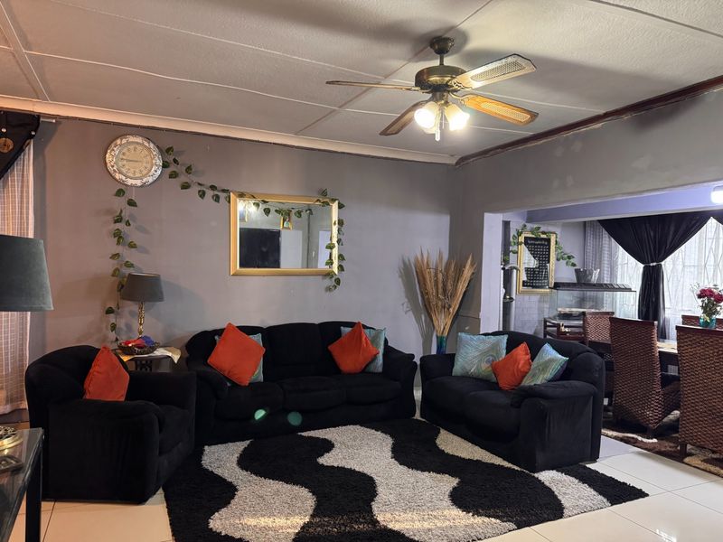 A living room featuring tiled flooring and a ceiling fan, with an open-plan layout connecting to the adjacent dining area.