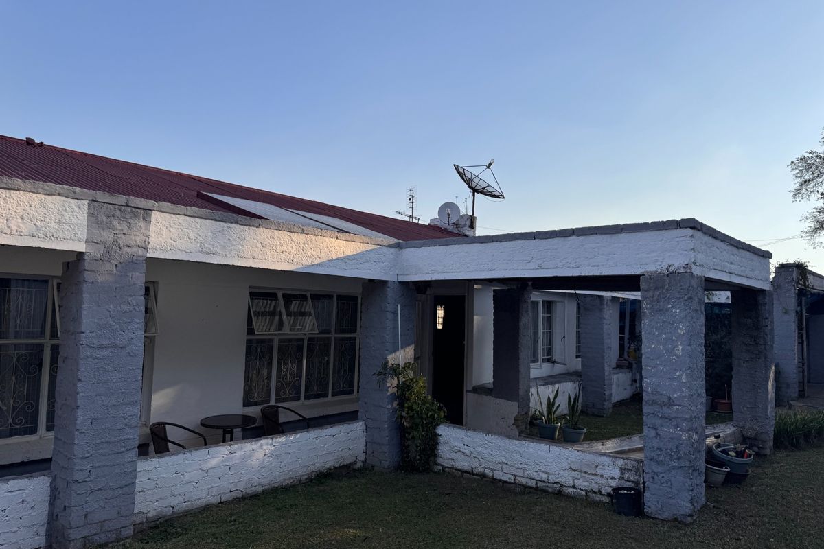 A rear view of the house featuring a covered patio area with brick pillars and a metal roof, set against a lawn.
