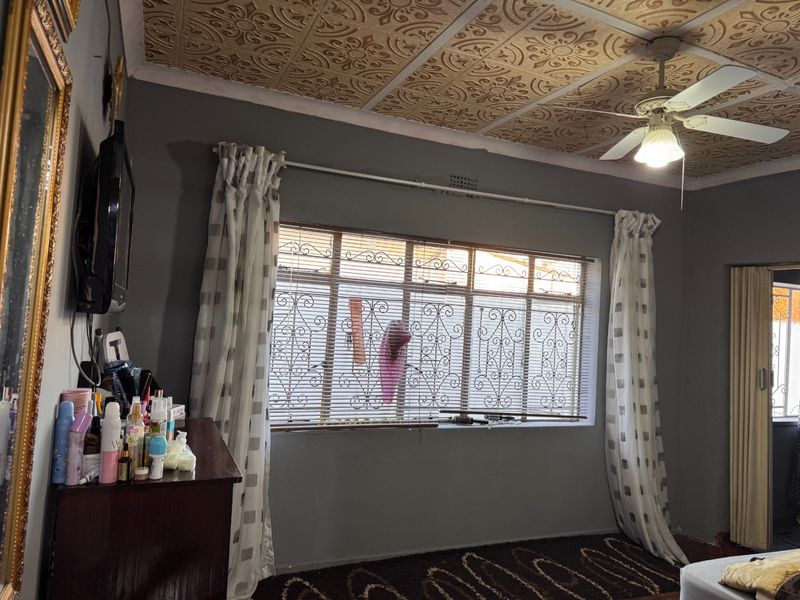 A bedroom featuring decorative ceiling tiles, a ceiling fan, and a window fitted with security bars.