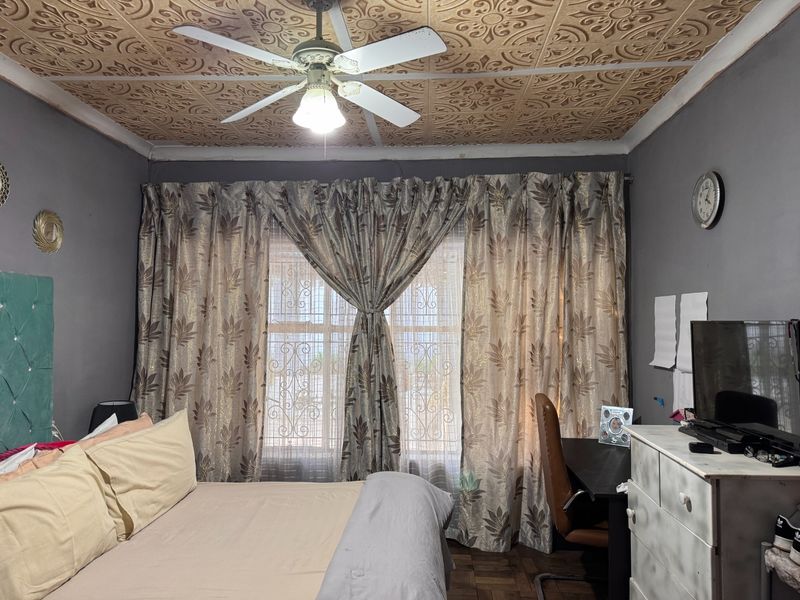 A bedroom featuring decorative ceiling tiles, a ceiling fan, parquet flooring, and windows fitted with security bars.