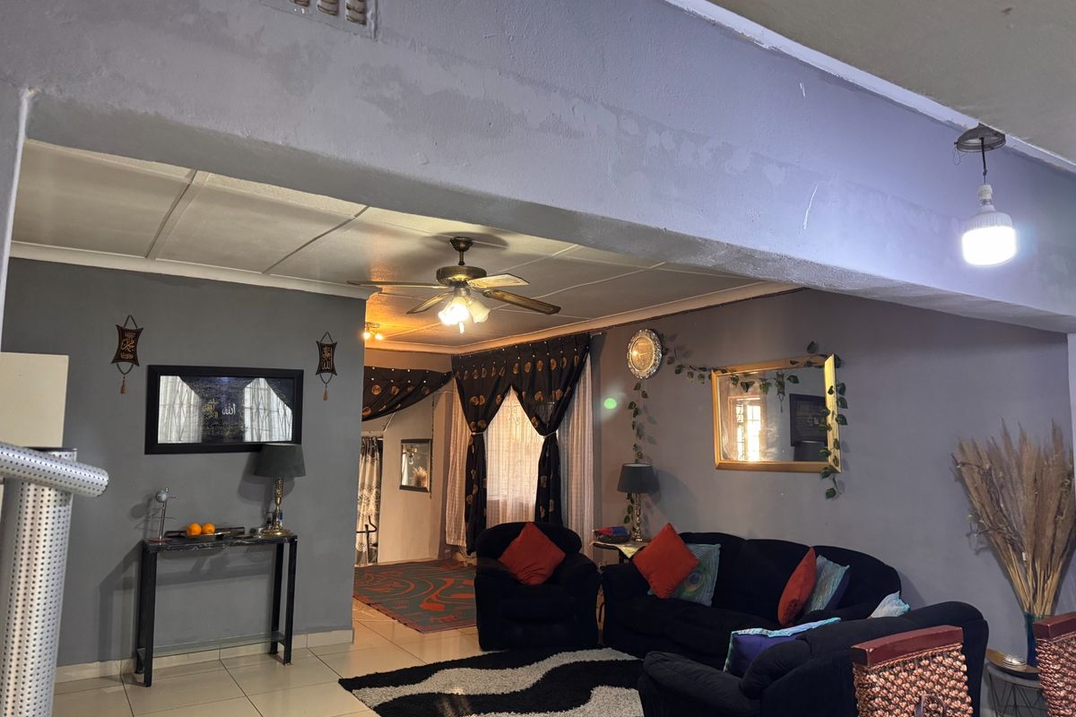 A living room area featuring tiled flooring, a ceiling fan, and an open-plan layout with an archway connecting to adjacent spaces.