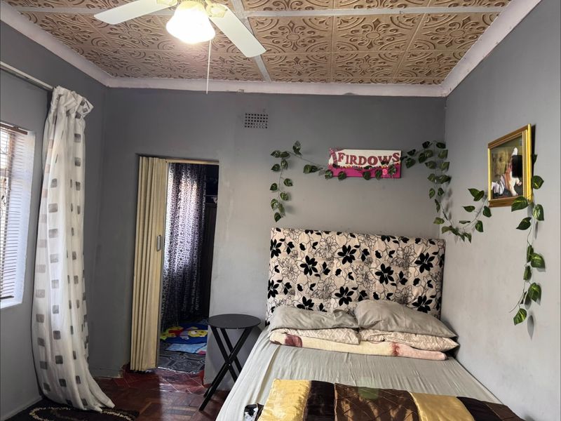 A bedroom featuring decorative ceiling tiles, a ceiling fan, and parquet flooring, with a folding door leading to an adjacent space.