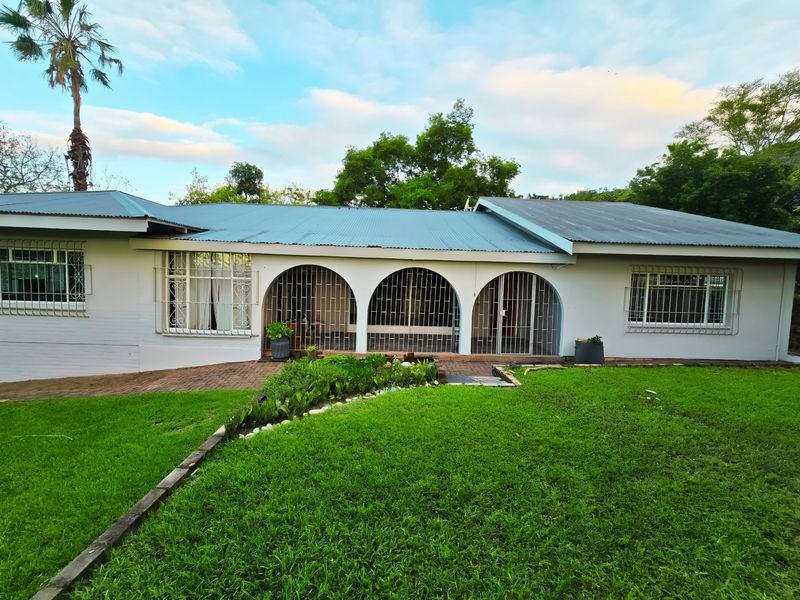 Rear view of a single-story house featuring a corrugated metal roof, arched patio area with security bars, and a well-maintained lawn.