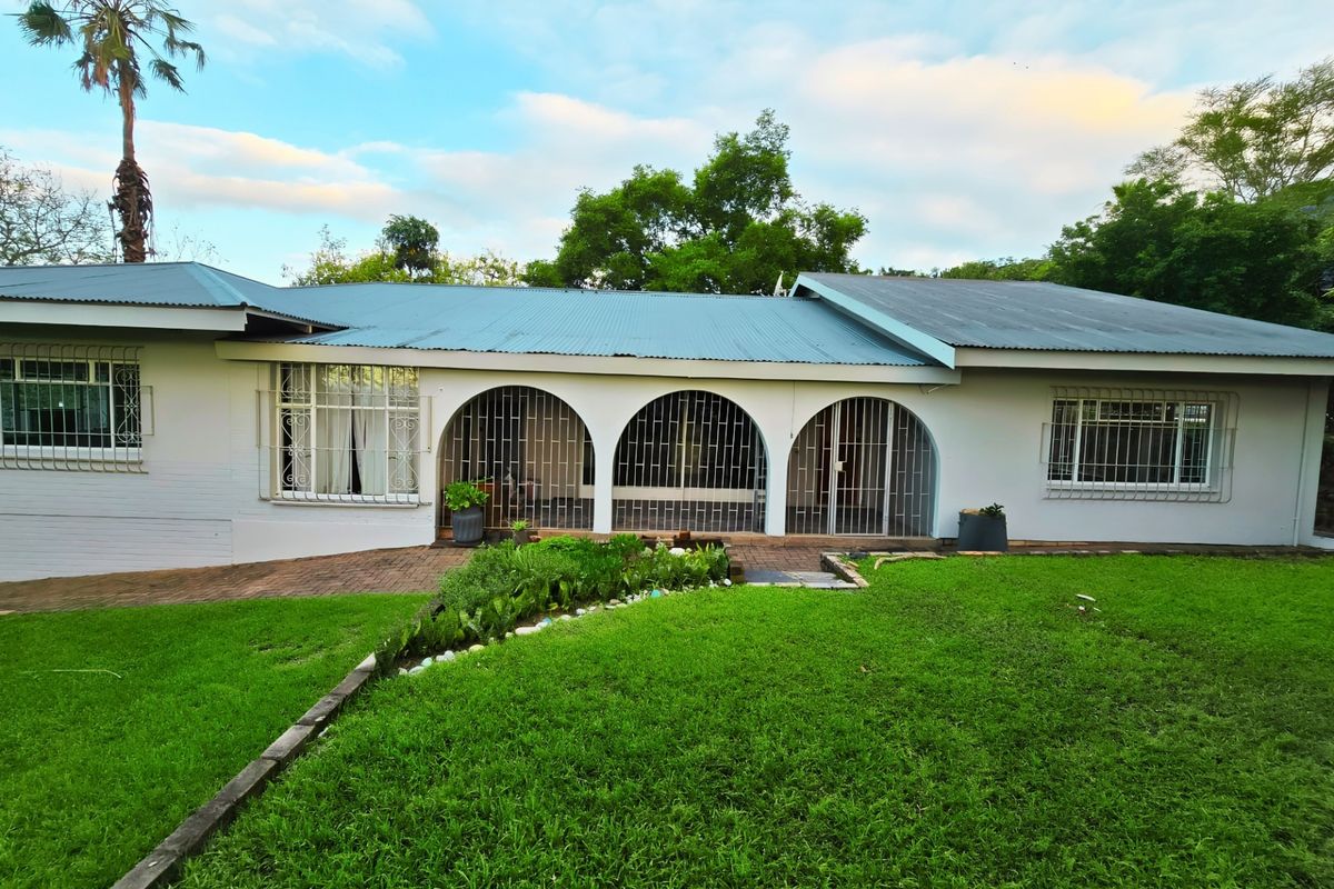 Rear view of a single-story house featuring a corrugated metal roof, arched patio area with security bars, and a well-maintained lawn.