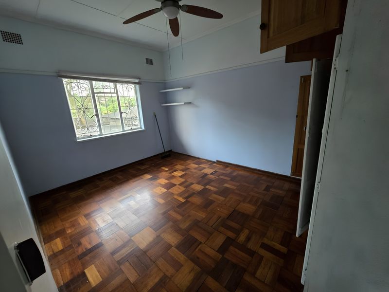 A spacious bedroom featuring original parquet flooring, a ceiling fan, and built-in storage, offering a blank canvas for personalization.