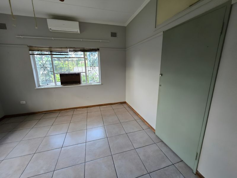 An empty bedroom featuring tiled flooring, a split-system air conditioner, and a window with security bars.
