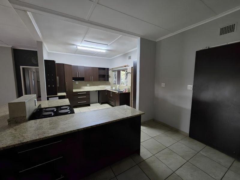 Open plan kitchen featuring dark wood cabinetry, granite countertops, and an integrated electric hob, with neutral tiled flooring throughout the space.