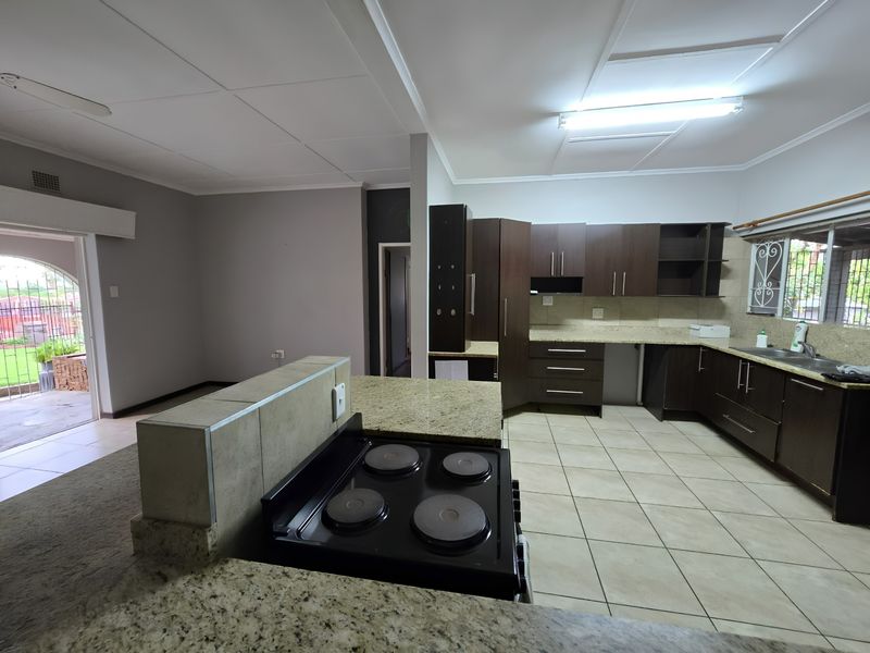Open plan kitchen featuring dark cabinetry, granite countertops, and an integrated electric hob, flowing into an adjacent living area with direct patio access.