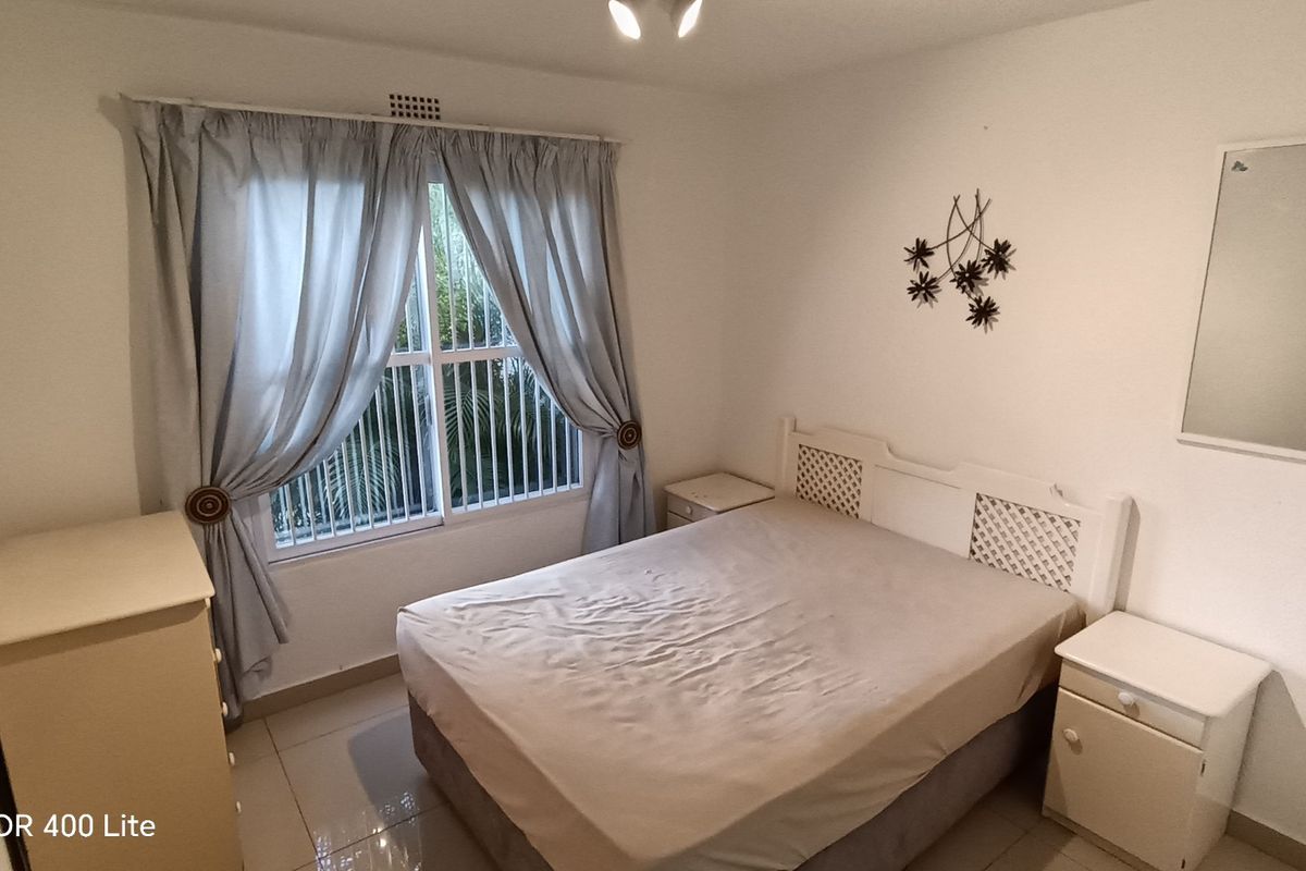 A functional bedroom featuring tiled flooring, a window with security bars, and neutral wall finishes.