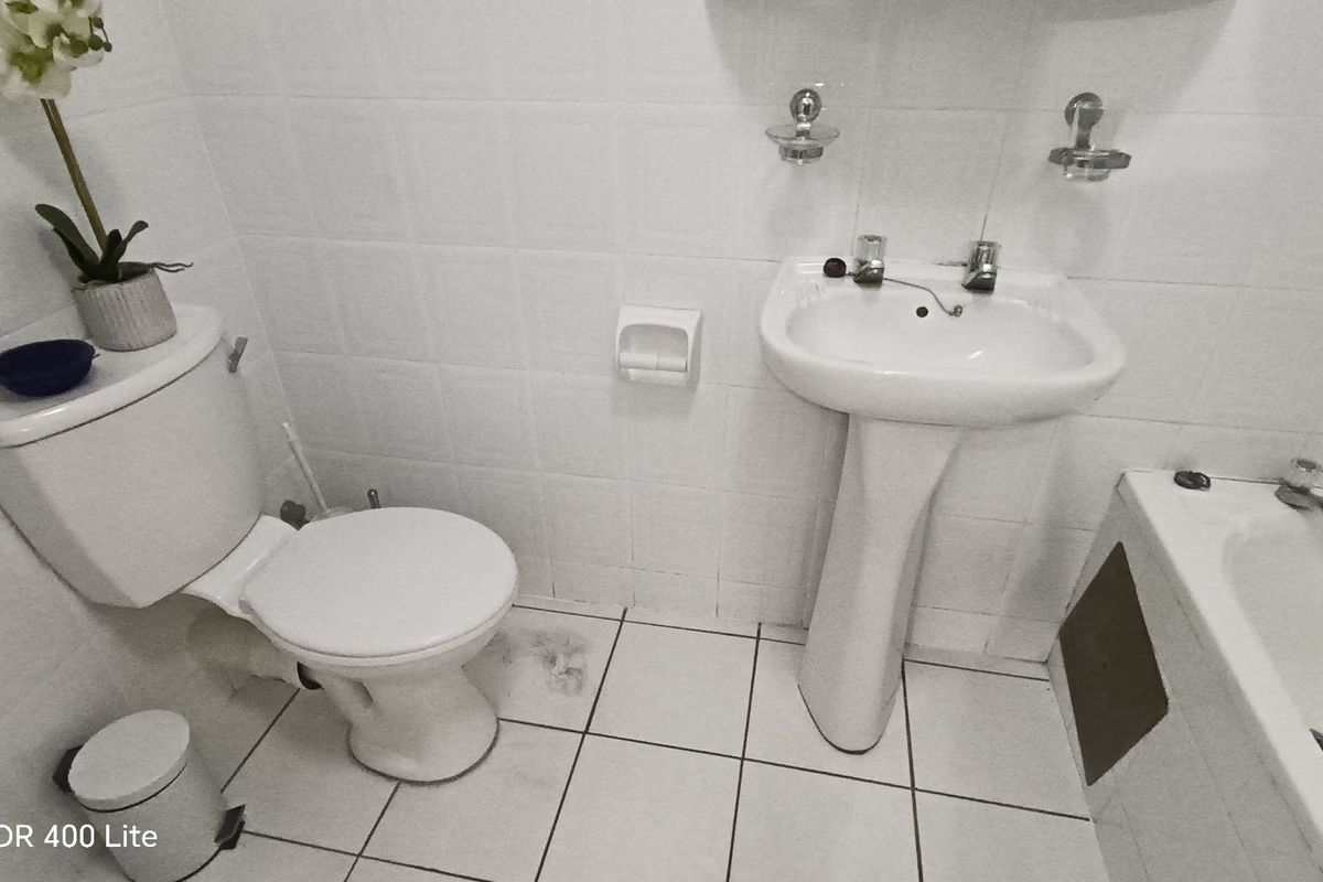 A functional bathroom featuring a white pedestal sink, standard toilet, and a bathtub with tiled walls and flooring.