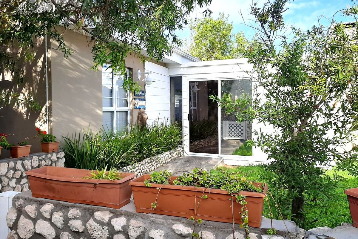 A view of the exterior rear facade featuring a paved walkway, sliding glass doors, and stone-clad retaining walls with landscaped garden beds.