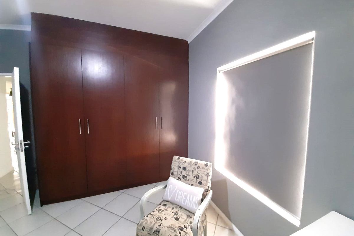 A bedroom featuring built-in wooden cabinetry and tiled flooring, illuminated by a window with a roller blind.