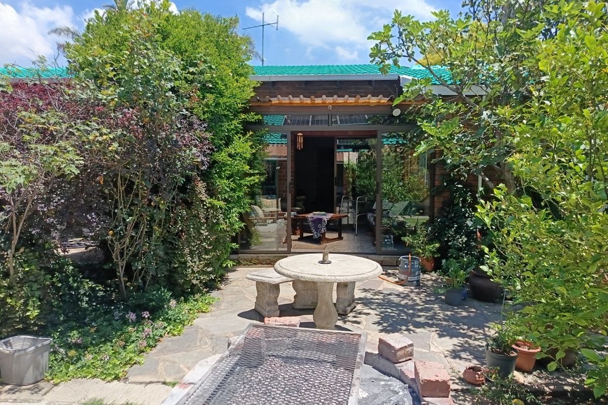 A private rear garden featuring a stone-paved patio, a built-in brick braai, and a covered outdoor area with sliding glass doors leading inside.