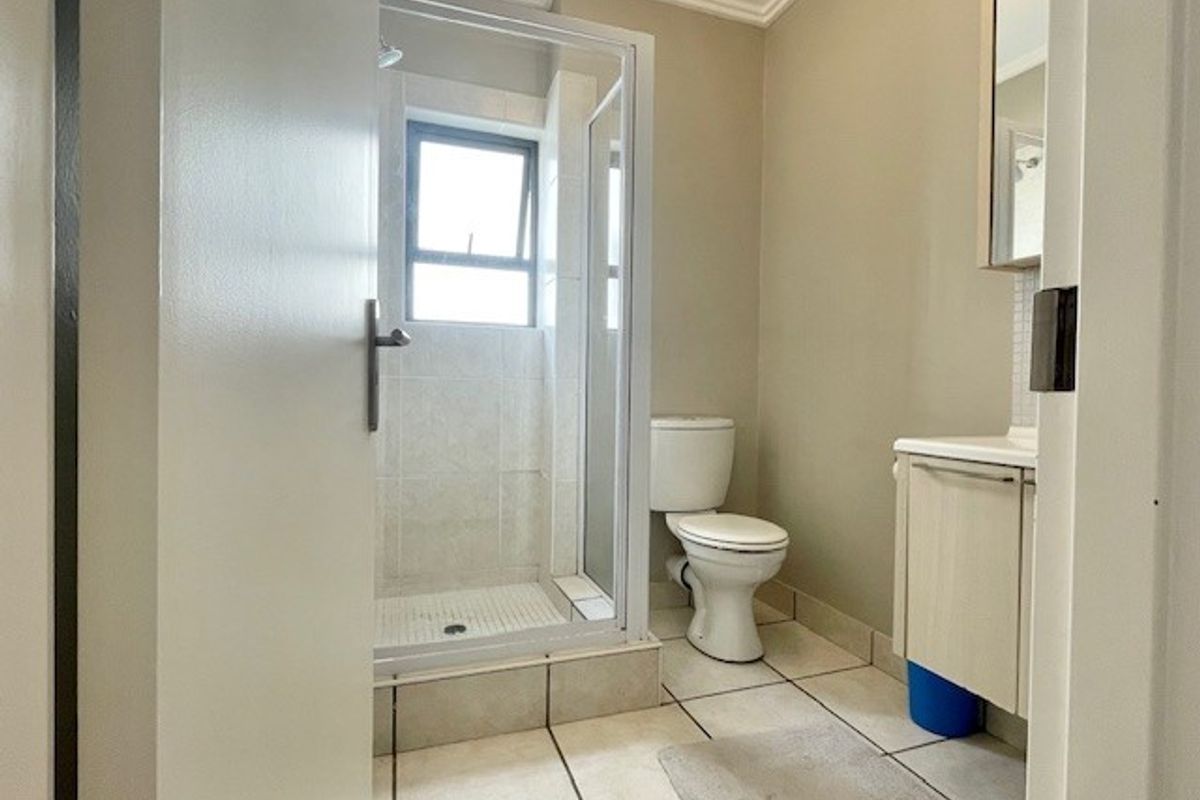 A functional bathroom featuring a glass-enclosed shower, a standard toilet, and a built-in vanity cabinet with a mirror.