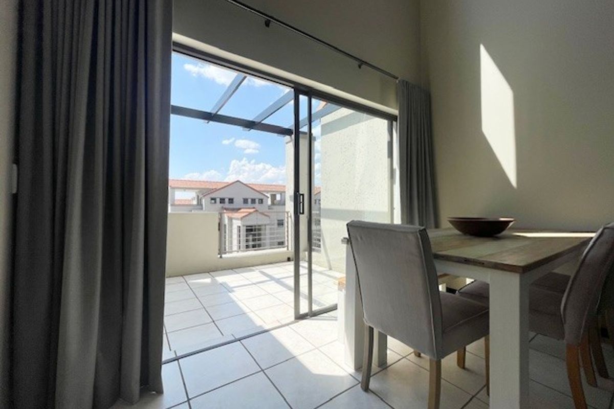 Bright living area featuring large sliding glass doors that open onto a tiled balcony with a pergola structure.