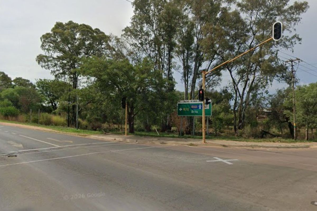 A street-level view of the intersection adjacent to the vacant agricultural land, showing road infrastructure and surrounding mature trees.