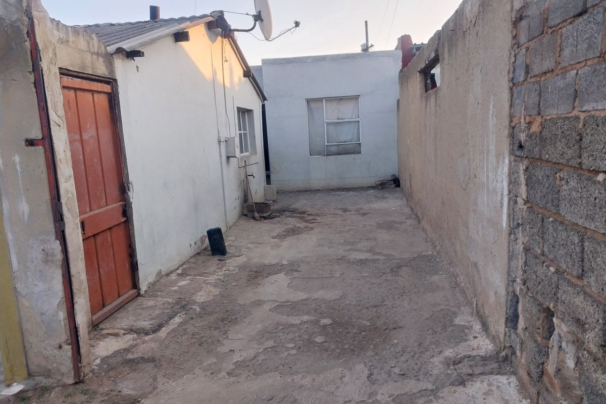 A narrow exterior rear courtyard area featuring concrete paving, exposed brick boundary walls, and access to the main dwelling structure.
