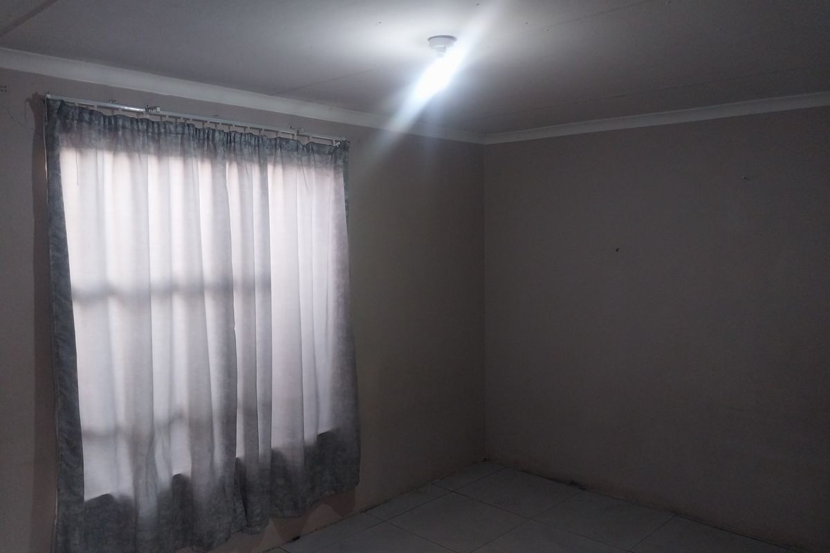 A simple, empty bedroom featuring tiled flooring, neutral walls, and a window with fitted curtain rails.