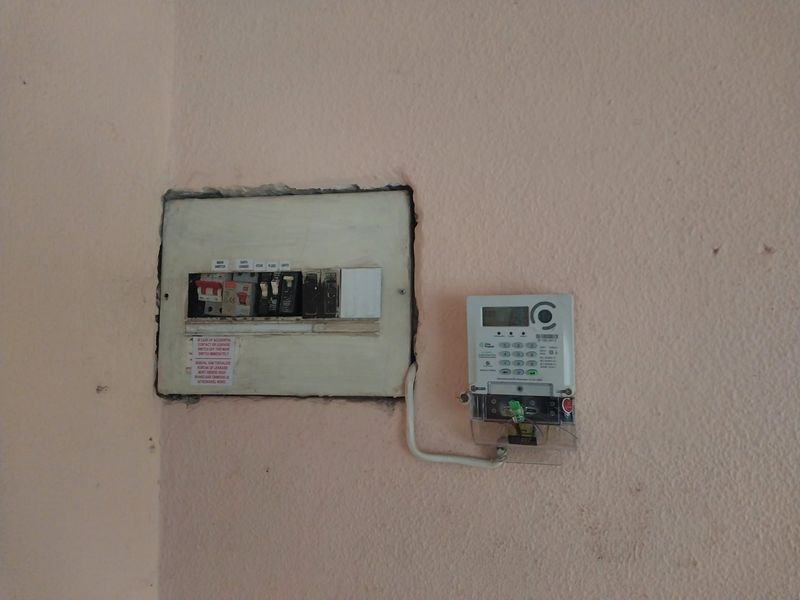Wall-mounted electrical distribution board and digital prepaid electricity meter installed on a painted interior wall.