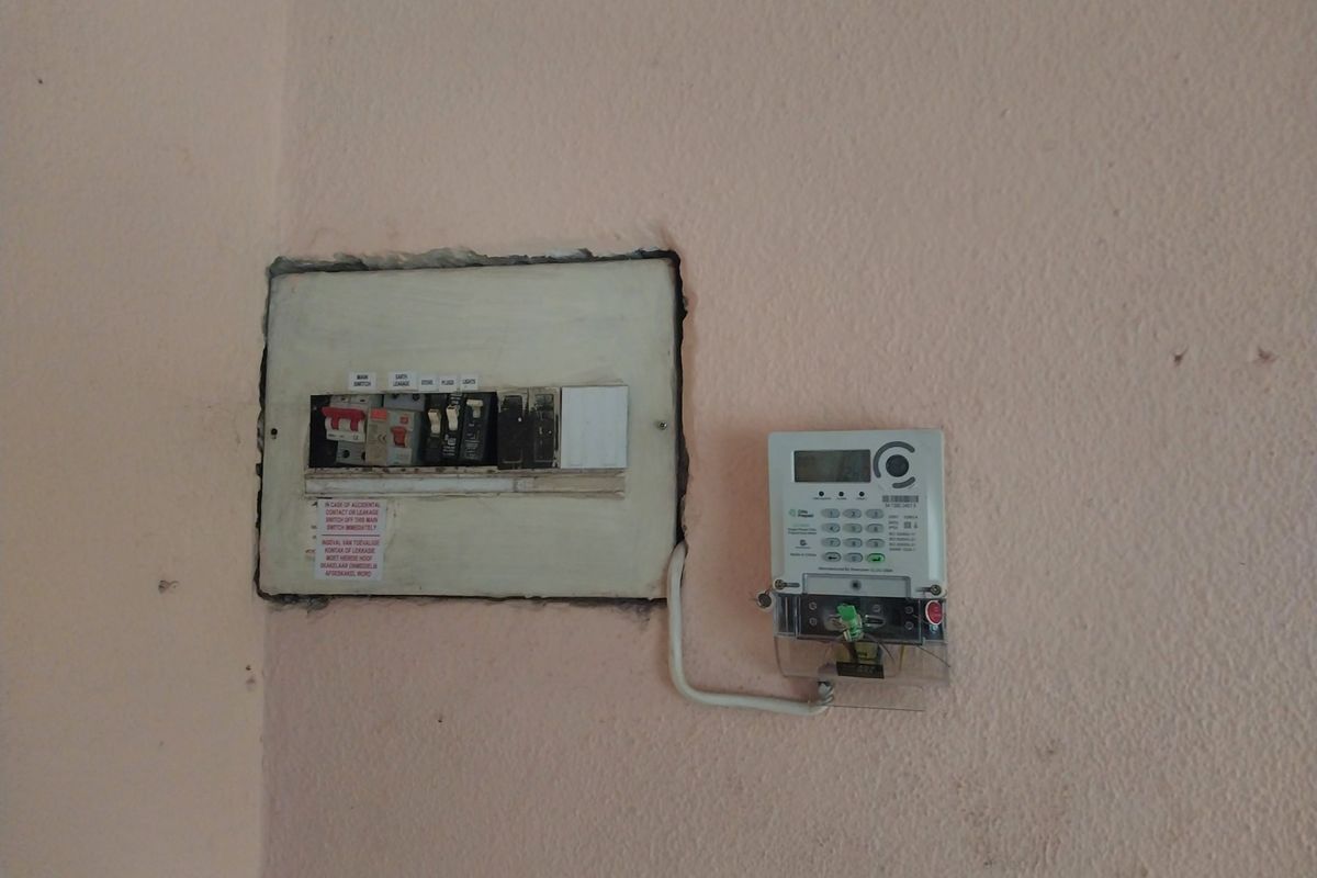 Wall-mounted electrical distribution board and digital prepaid electricity meter installed on a painted interior wall.