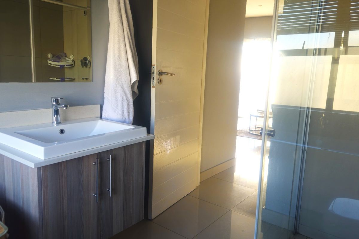 Modern bathroom featuring a vanity with basin, mixer tap, and a glass-enclosed shower with tiled flooring.