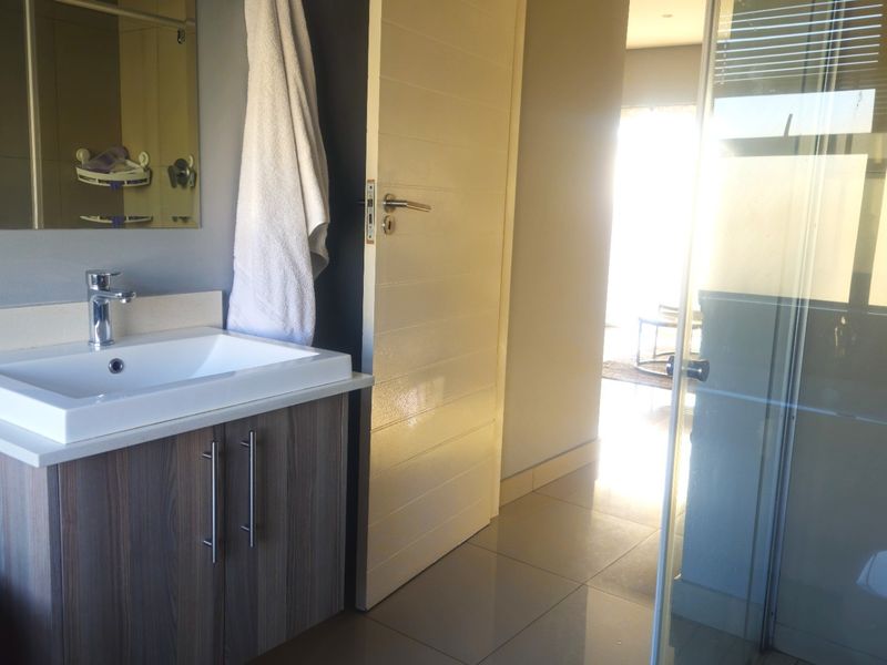 Modern bathroom featuring a vanity with basin, mixer tap, and a glass-enclosed shower with tiled flooring.