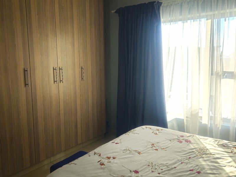 A bedroom featuring floor-to-ceiling wood-finish built-in cupboards and a window with curtains.