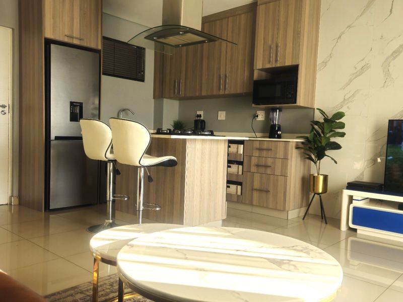 Modern open-plan living area featuring a contemporary kitchen with wood-finish cabinetry, integrated appliances, and stylish marble-look wall accents.