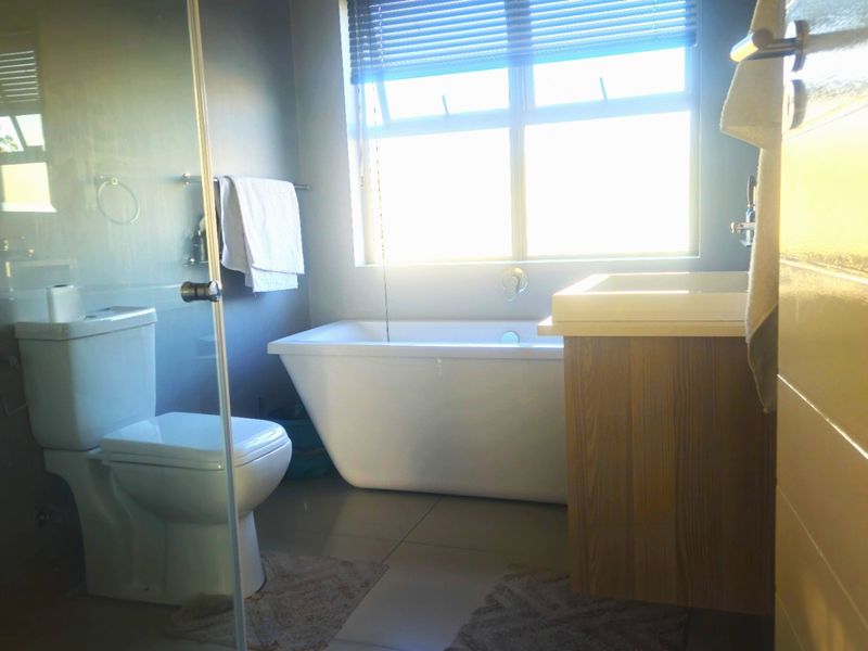 Modern bathroom featuring a freestanding bathtub, glass-enclosed shower, and a wooden vanity cabinet with a basin.