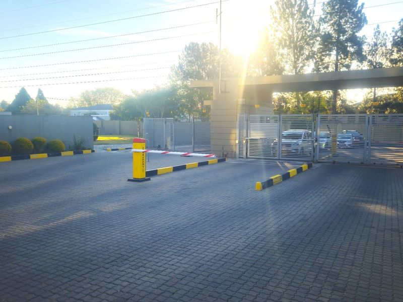 Secure gated entrance to the apartment complex featuring a paved driveway, automated boom gate, and perimeter security fencing.
