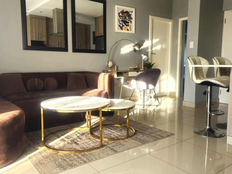 Modern open-plan living area featuring polished porcelain floor tiles, a breakfast bar, and neutral wall finishes, creating a bright and cohesive living space.