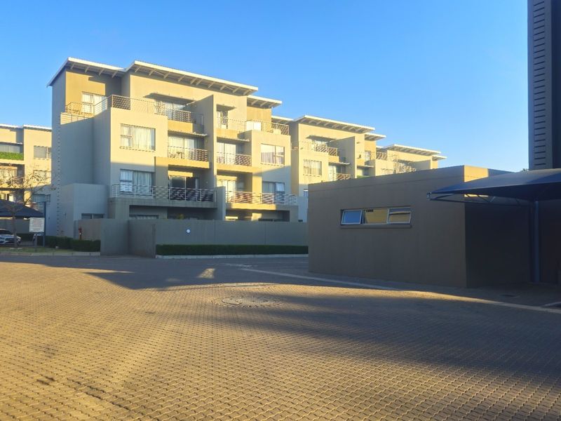 Exterior view of a modern multi-story apartment complex featuring paved driveway access and covered parking structures.
