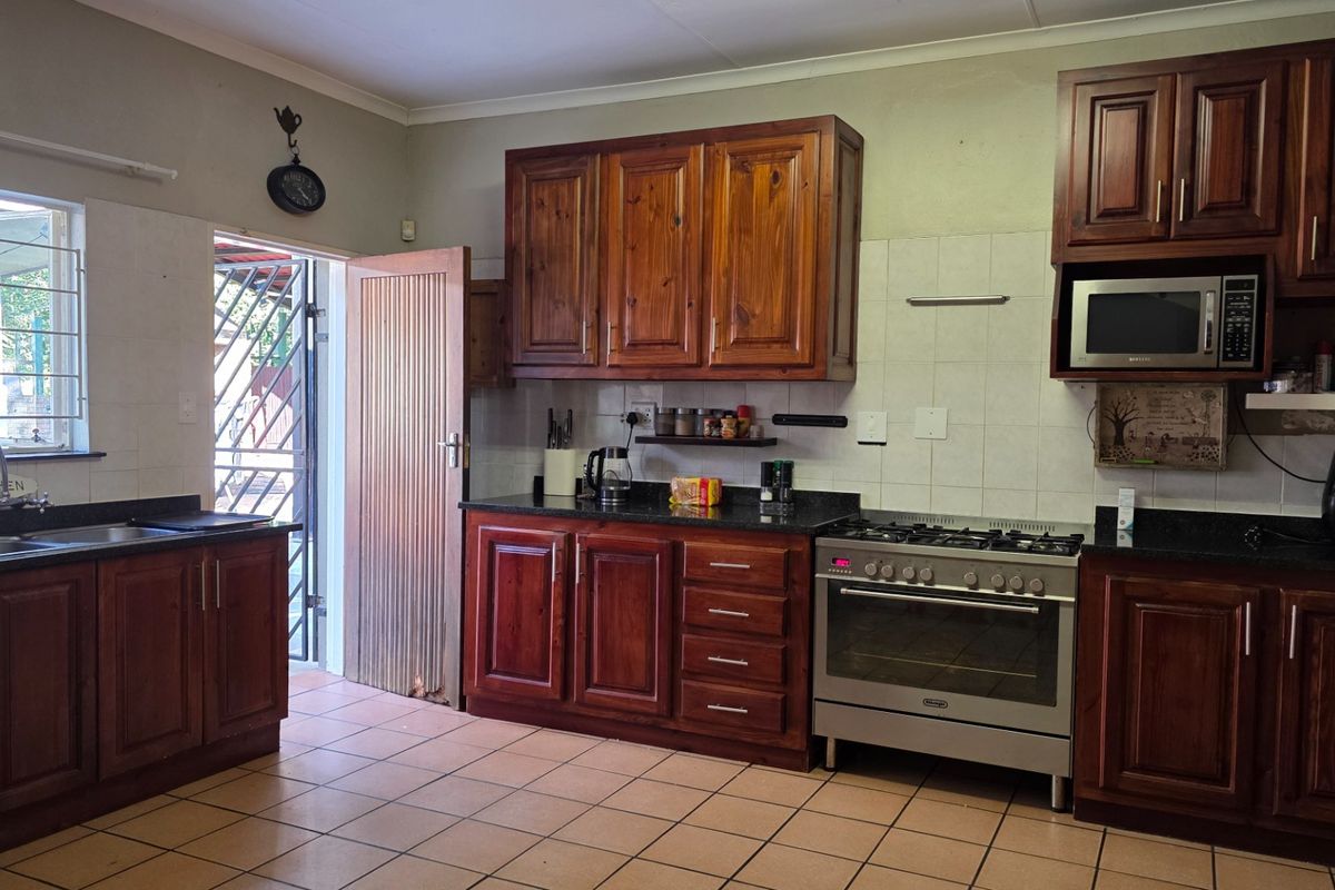 A functional kitchen featuring wooden cabinetry, granite countertops, a stainless steel gas stove, and direct access to the exterior via a security gate.