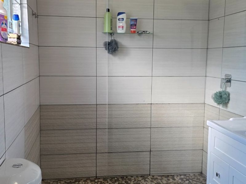 Modern bathroom featuring a walk-in shower with a pebble floor, glass screen, rain shower head, and a white vanity cabinet.