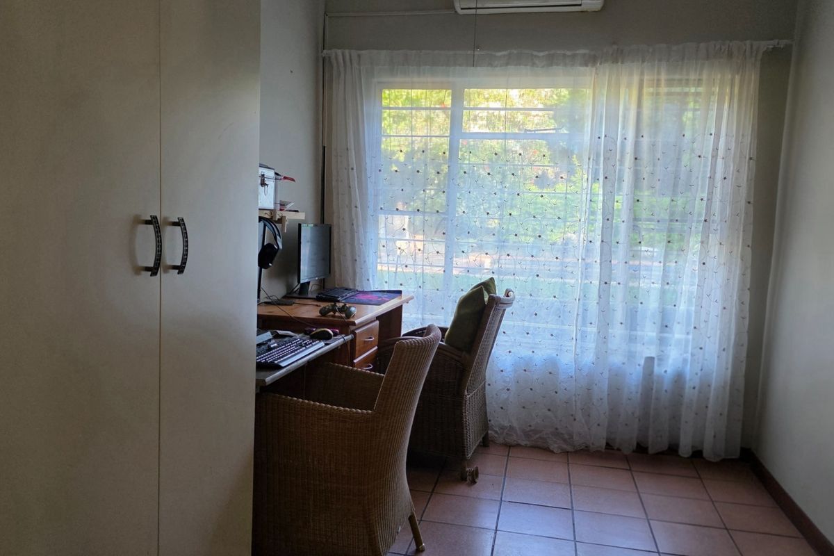 A functional bedroom featuring tiled flooring, a built-in wardrobe, and an air conditioning unit, with natural light streaming through a large window.