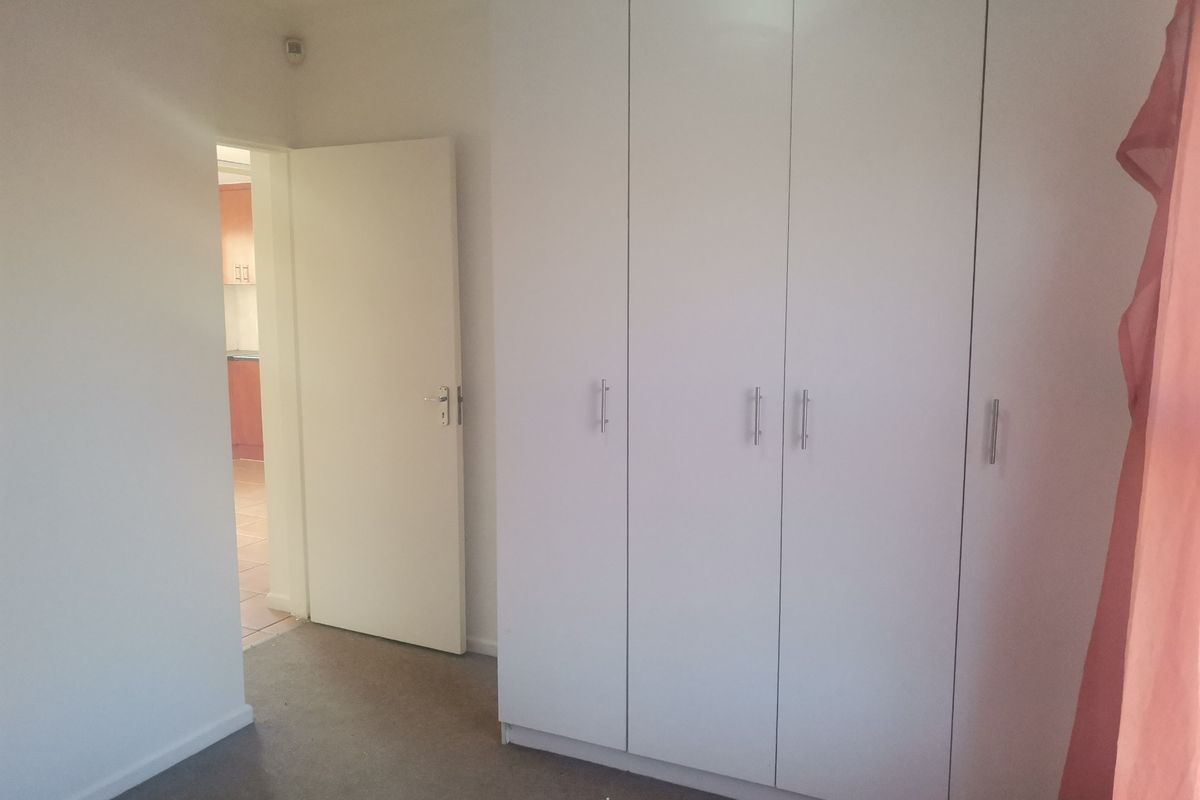 A bedroom featuring built-in white cabinetry and carpeted flooring, with a doorway leading to an adjacent room.