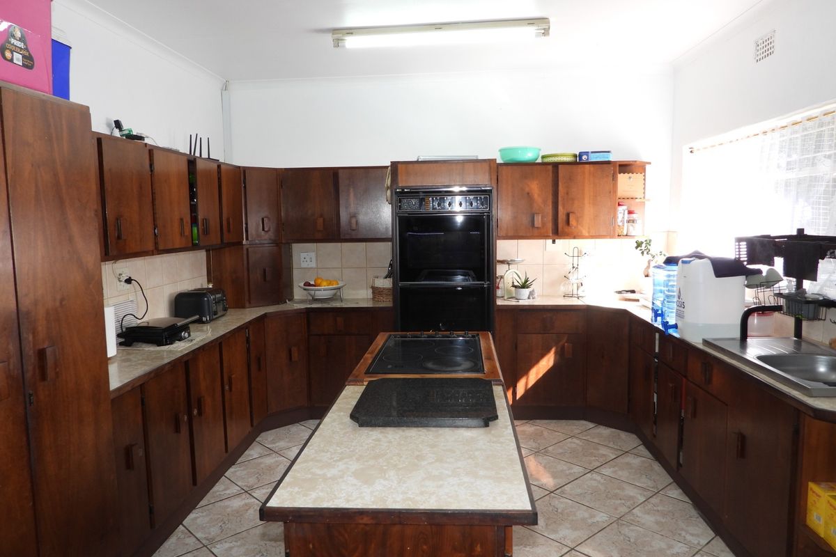 Spacious kitchen featuring extensive dark wood cabinetry, a central island with a built-in cooktop, double wall oven, and tiled flooring.