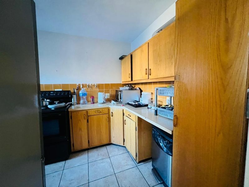 A dated kitchen featuring wood-look laminate cabinetry, ceramic tile backsplash, and tiled flooring, offering potential for a modern renovation.