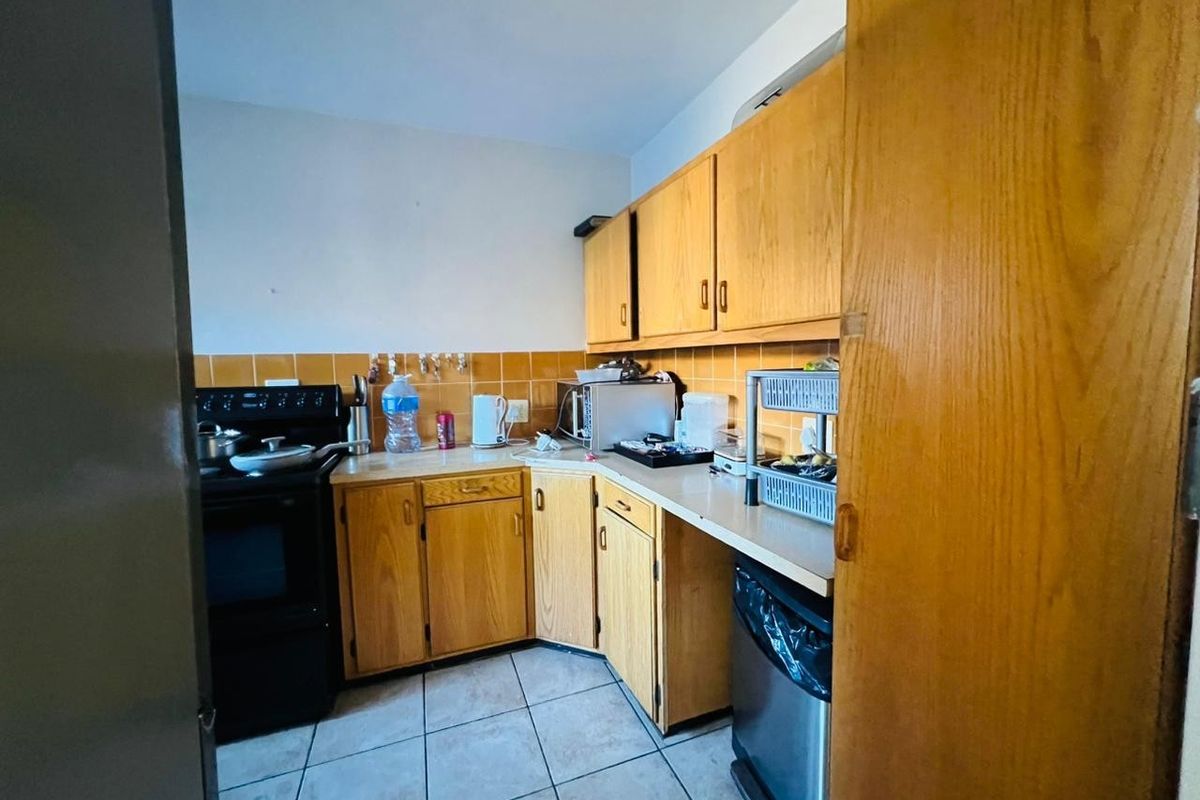 A dated kitchen featuring wood-look laminate cabinetry, ceramic tile backsplash, and tiled flooring, offering potential for a modern renovation.
