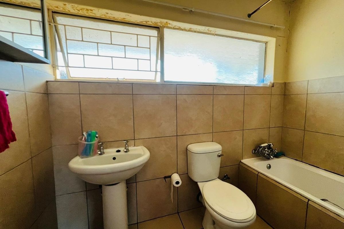A functional bathroom featuring a pedestal basin, toilet, and bathtub with tiled walls and flooring, requiring cosmetic updates to the window frames and finishes.