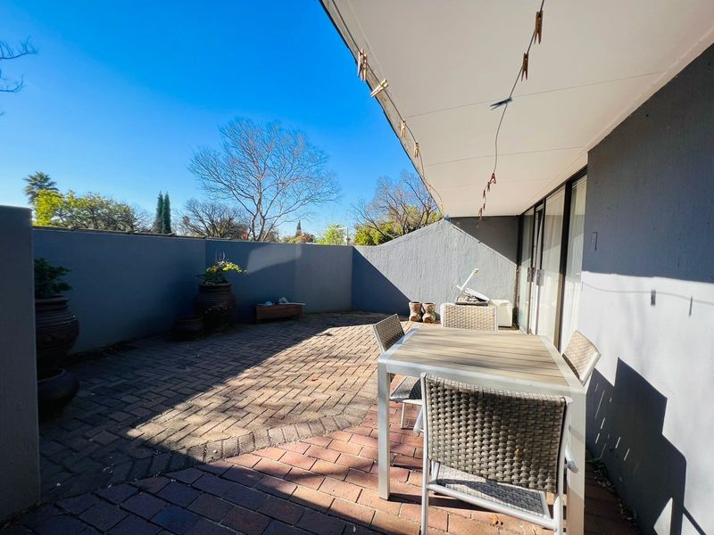 A private paved patio area featuring a covered section, ideal for outdoor dining and relaxation, accessible via sliding glass doors.