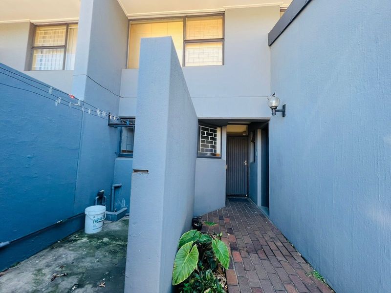 A private entrance area featuring brick paving, a privacy wall, and exterior lighting, leading to the main townhouse doorway.