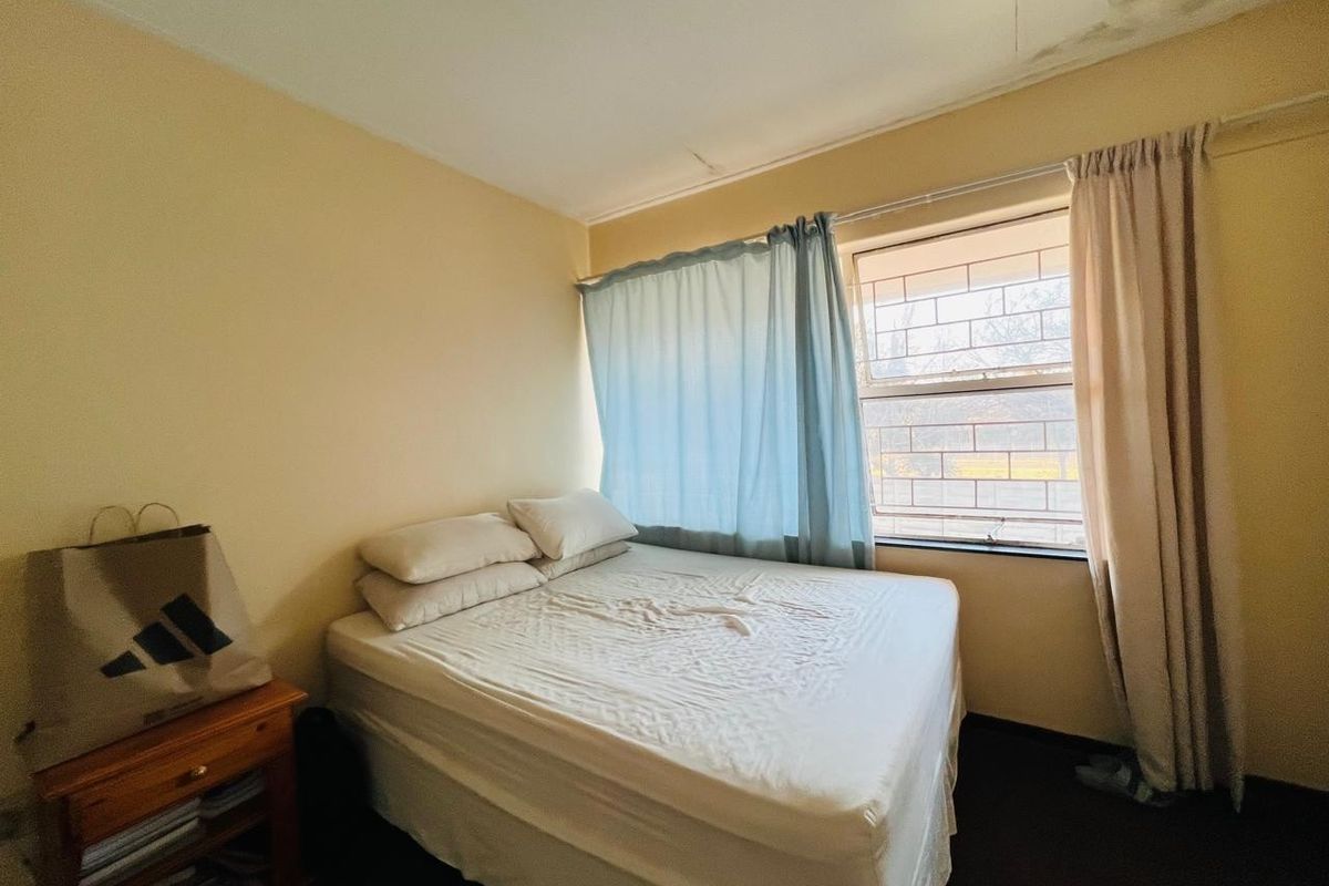 A bedroom featuring a window with security bars and visible ceiling damage requiring repair.